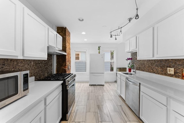 kitchen with appliances with stainless steel finishes, a sink, under cabinet range hood, white cabinetry, and tasteful backsplash