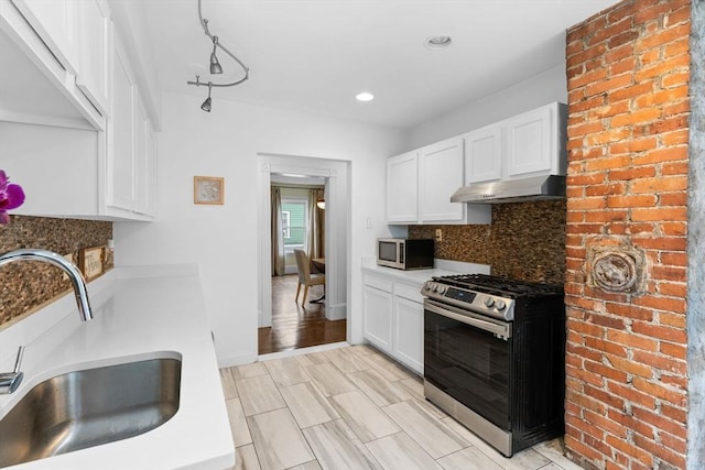 kitchen with stainless steel appliances, under cabinet range hood, a sink, white cabinetry, and decorative backsplash