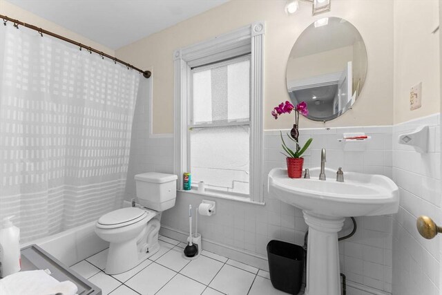 full bathroom featuring tile walls, tile patterned floors, wainscoting, curtained shower, and toilet