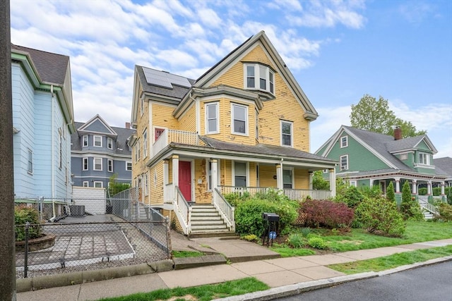 victorian home featuring covered porch, roof mounted solar panels, and fence
