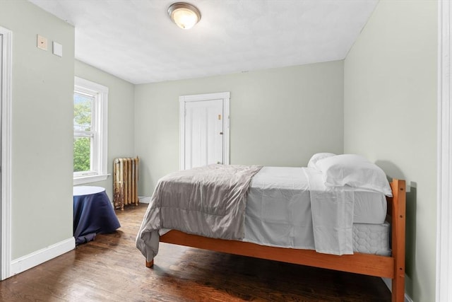 bedroom with radiator heating unit, wood finished floors, and baseboards