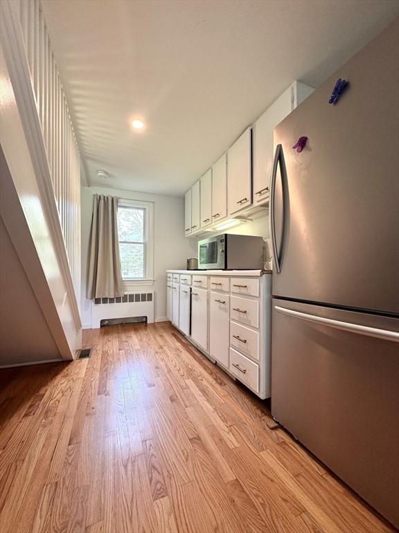 84 Walden Ter, Concord, MA 01742 - kitchen featuring stainless steel appliances, radiator, light wood-style flooring, and white cabinets