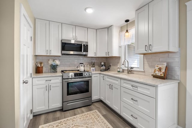 kitchen with a sink, wood finished floors, stainless steel appliances, white cabinets, and light stone countertops