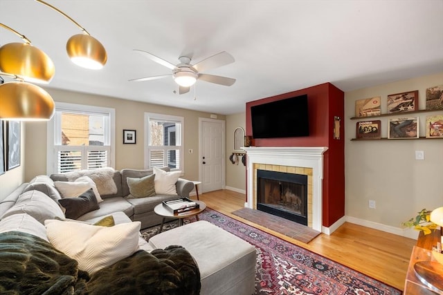 living room featuring baseboards, wood finished floors, a ceiling fan, and a tile fireplace