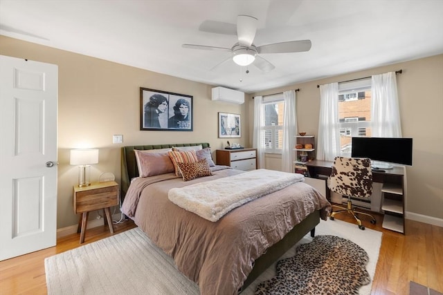 bedroom featuring light wood finished floors, a wall mounted air conditioner, baseboards, and a ceiling fan