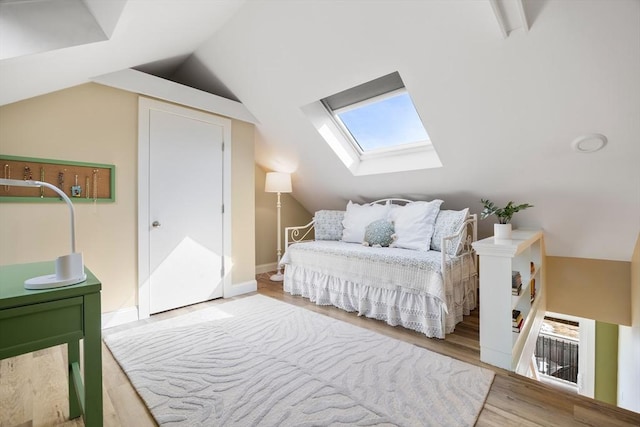 bedroom featuring lofted ceiling with skylight, baseboards, and wood finished floors