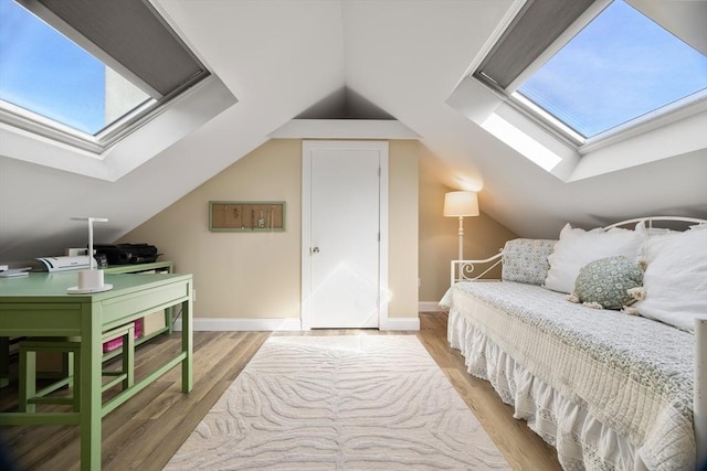 bedroom featuring lofted ceiling with skylight, light wood-style flooring, and baseboards