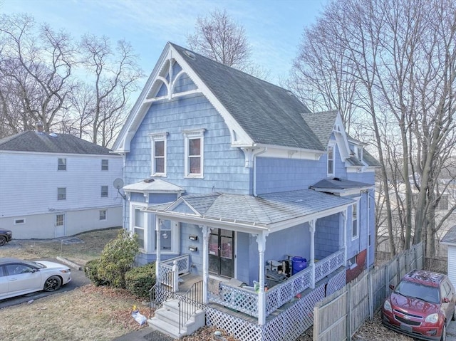 view of front facade with roof with shingles, a porch, and fence