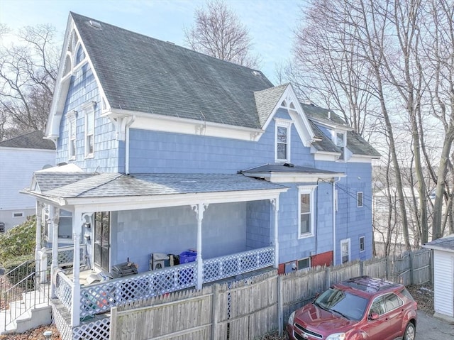 rear view of property with a porch, roof with shingles, and fence