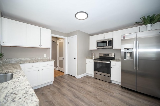 kitchen featuring hardwood / wood-style flooring, white cabinetry, appliances with stainless steel finishes, and light stone counters