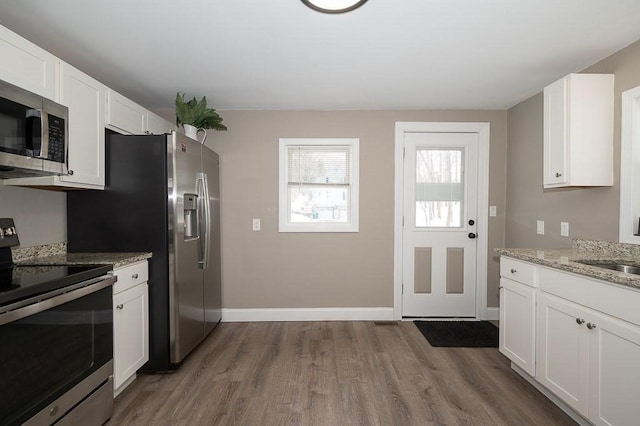 kitchen featuring dark wood-type flooring, sink, light stone counters, appliances with stainless steel finishes, and white cabinets