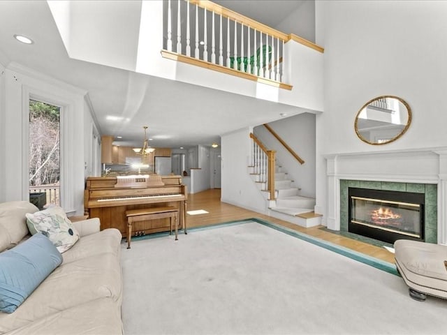 carpeted living room with wood finished floors, recessed lighting, a tile fireplace, stairs, and a towering ceiling