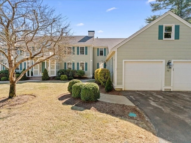 view of front of house featuring driveway, a chimney, a garage, and a front yard