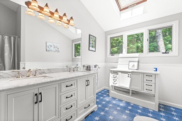 75 Winter St, Hopkinton, MA 01748 - bathroom featuring tile patterned floors, a skylight, vaulted ceiling, double vanity, and wainscoting