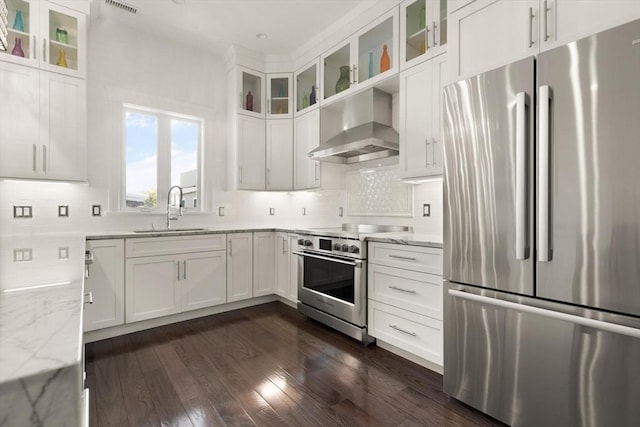 125 Heath St, Somerville, MA 02145 - kitchen featuring appliances with stainless steel finishes, wall chimney range hood, light stone countertops, and white cabinetry