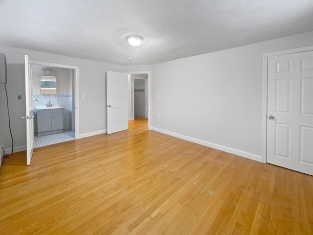 unfurnished bedroom with light hardwood / wood-style floors, sink, and ensuite bathroom