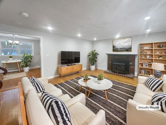 living room featuring a wood stove, wood-type flooring, a baseboard heating unit, and a notable chandelier