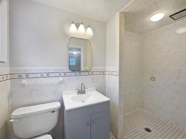 bathroom featuring toilet, tiled shower, tile walls, a textured ceiling, and vanity