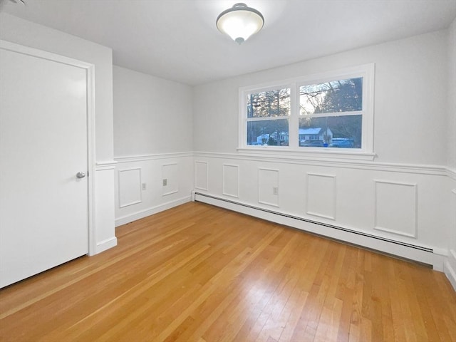 unfurnished room featuring a baseboard heating unit and light wood-type flooring