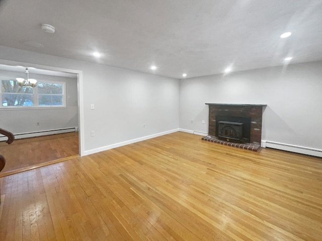 unfurnished living room with light wood-type flooring, baseboard heating, an inviting chandelier, and a wood stove