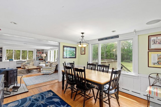 dining space with a healthy amount of sunlight, a baseboard heating unit, a wood stove, and light wood-type flooring