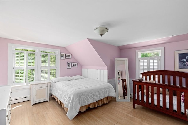 bedroom featuring a baseboard heating unit, vaulted ceiling, and light wood-type flooring