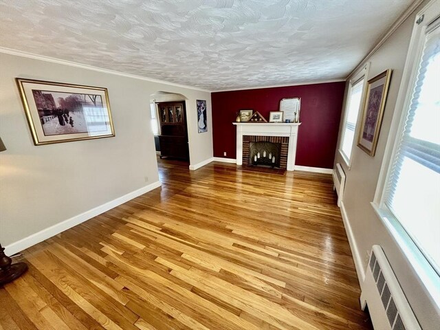 unfurnished living room with arched walkways, light wood-style floors, a fireplace, crown molding, and baseboards