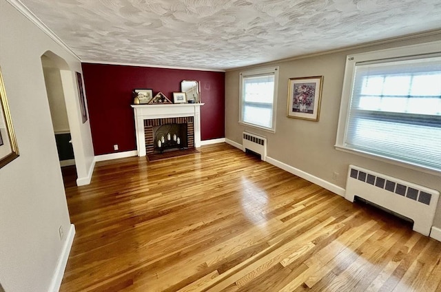 unfurnished living room with baseboards, arched walkways, wood finished floors, and radiator heating unit