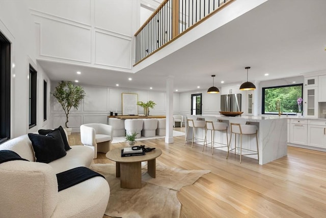 living room featuring recessed lighting, a decorative wall, a towering ceiling, and light wood finished floors