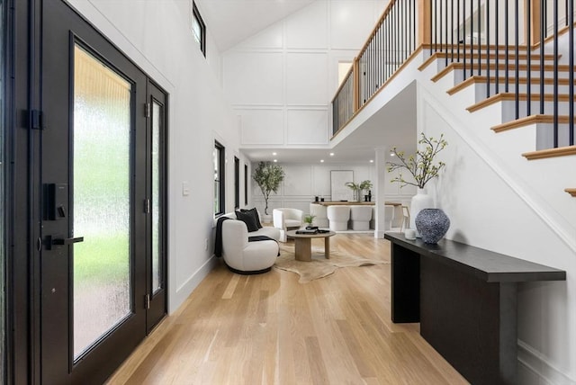 foyer featuring baseboards, a towering ceiling, light wood-style flooring, stairway, and a decorative wall