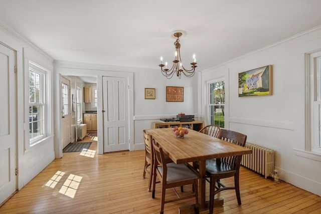 dining space with radiator, crown molding, light wood finished floors, a chandelier, and healthy amount of natural light