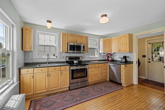 kitchen featuring stainless steel appliances, a sink, light brown cabinets, and radiator