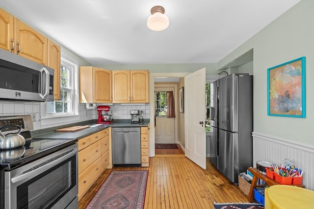 kitchen with stainless steel appliances, light brown cabinetry, dark countertops, light wood-style floors, and tasteful backsplash