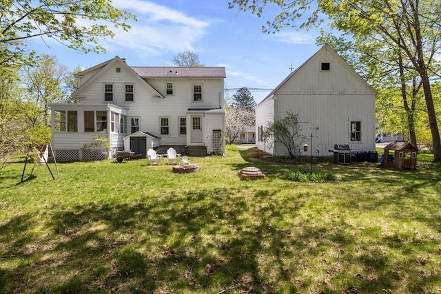 rear view of house featuring an outdoor fire pit, a storage shed, a sunroom, an outdoor structure, and a lawn