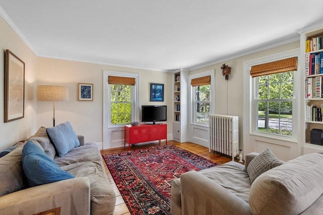 living area with radiator, plenty of natural light, built in shelves, crown molding, and wood finished floors