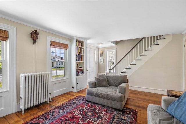 living area featuring radiator heating unit, hardwood / wood-style flooring, healthy amount of natural light, stairway, and ornamental molding