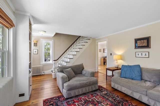 living area featuring radiator heating unit, light wood-type flooring, stairway, and crown molding