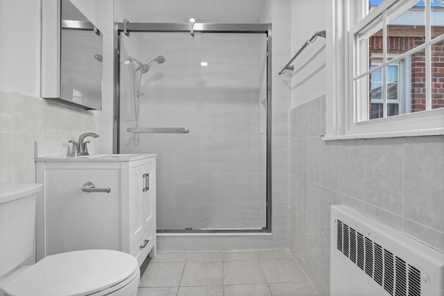 bathroom featuring radiator, tile patterned floors, toilet, a shower with door, and vanity