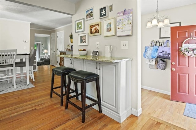 26 Gaslight Ln Unit 26, Easton, MA 02356 - kitchen with light wood-type flooring, a chandelier, a breakfast bar, baseboards, and crown molding
