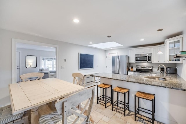 kitchen with a sink, a peninsula, appliances with stainless steel finishes, a skylight, and white cabinets