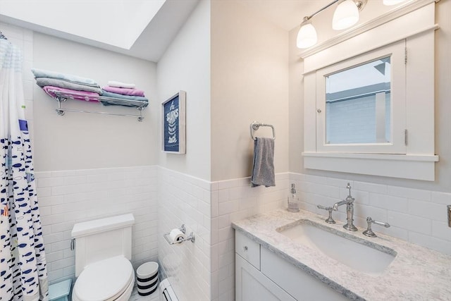 bathroom with toilet, tile walls, a skylight, wainscoting, and vanity