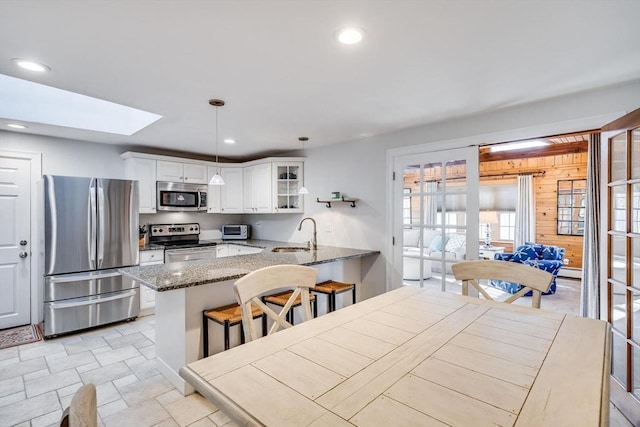 kitchen with a peninsula, a sink, stainless steel appliances, glass insert cabinets, and white cabinetry