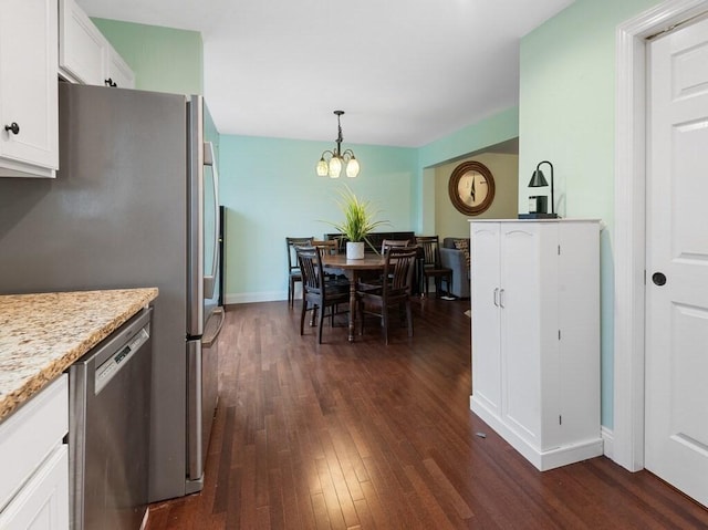 kitchen with appliances with stainless steel finishes, pendant lighting, dark hardwood / wood-style floors, white cabinets, and an inviting chandelier