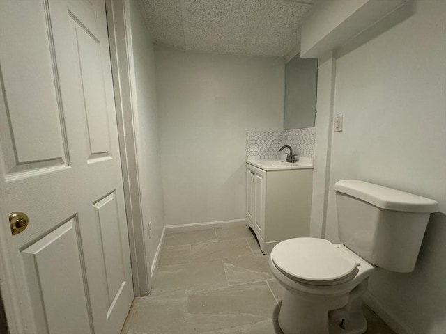 half bathroom featuring vanity, decorative backsplash, toilet, and baseboards