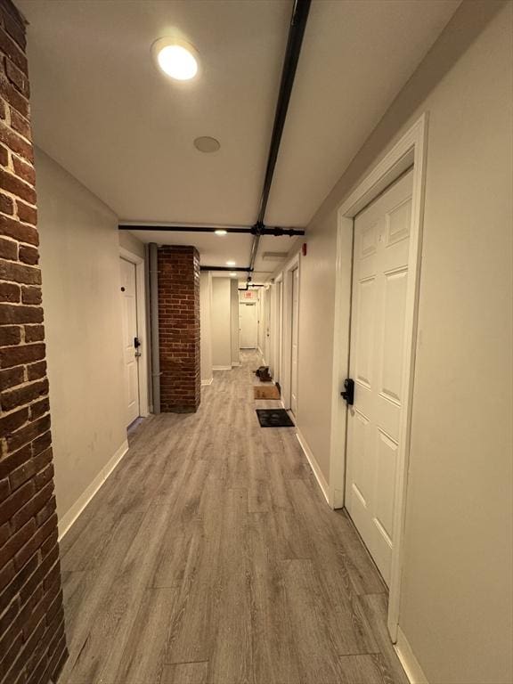 corridor featuring brick wall, wood finished floors, and baseboards