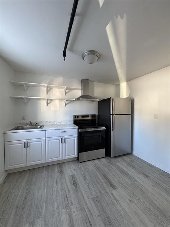 kitchen with light wood finished floors, stainless steel appliances, white cabinets, a sink, and wall chimney range hood