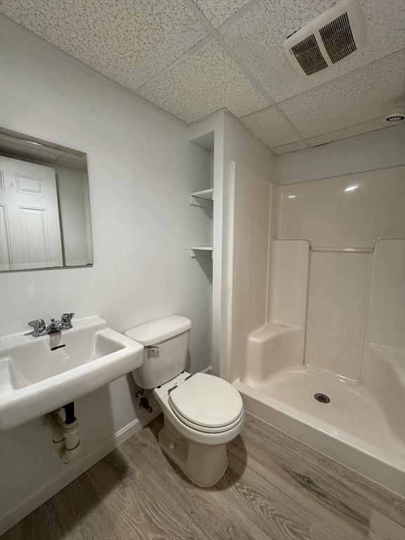 full bath featuring a drop ceiling, toilet, wood finished floors, visible vents, and a shower