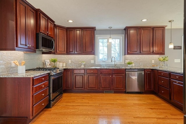 kitchen with light stone countertops, pendant lighting, light hardwood / wood-style floors, appliances with stainless steel finishes, and sink