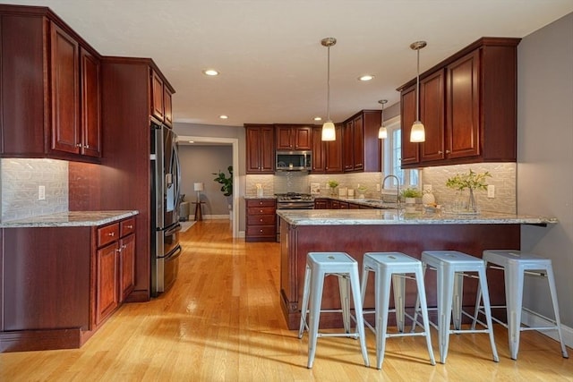 kitchen with a breakfast bar area, stainless steel appliances, kitchen peninsula, light hardwood / wood-style flooring, and decorative light fixtures