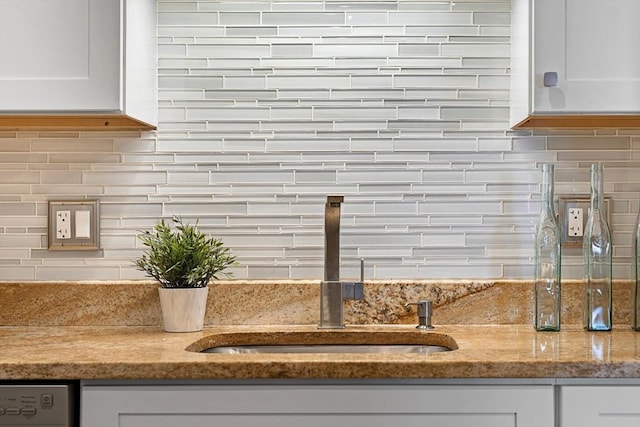 room details featuring sink, white cabinetry, decorative backsplash, and light stone counters